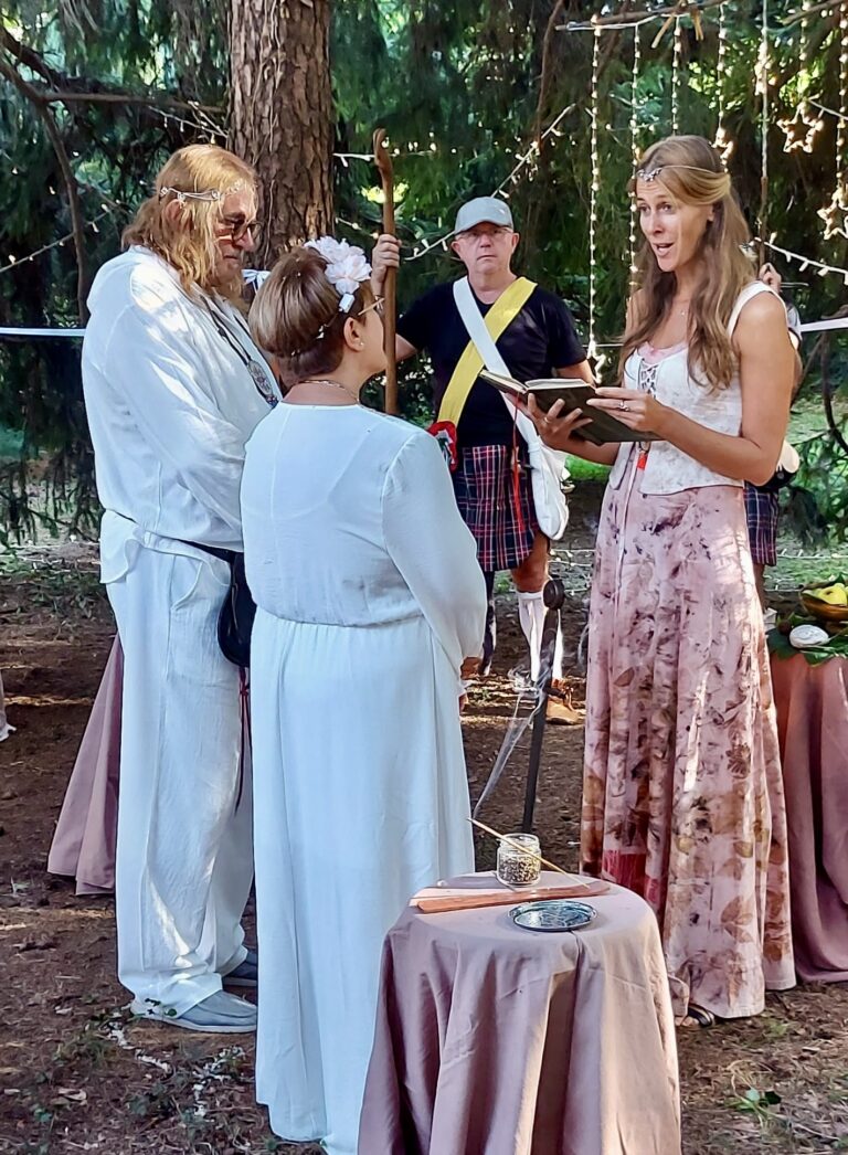 Una coppia vestita di bianco si sposa nel bosco con una celebrante