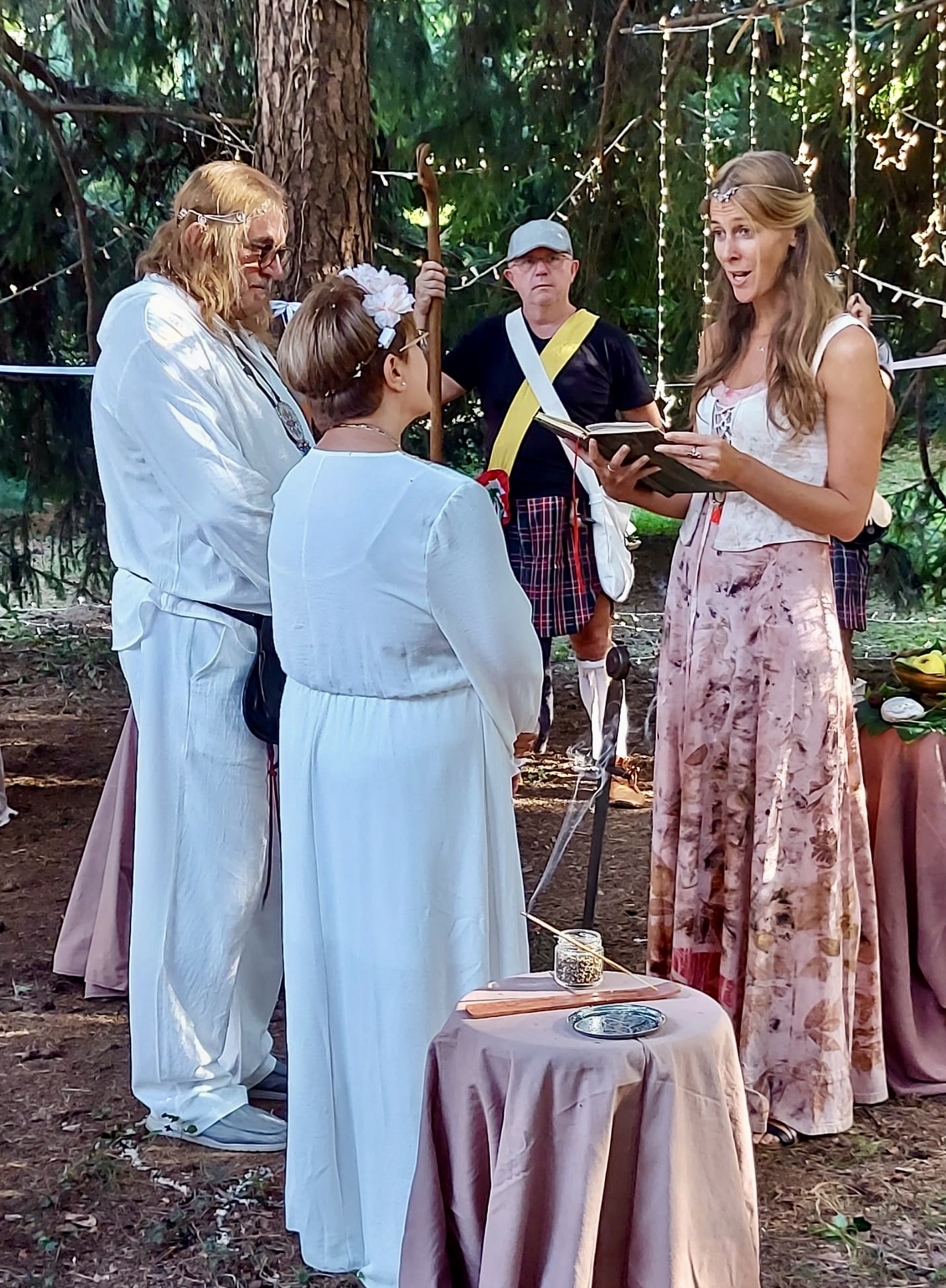 Una coppia vestita di bianco si sposa nel bosco con una celebrante